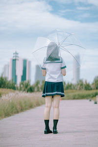 Rear view of young woman with umbrella standing on footpath