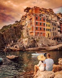 Rear view of people sitting by buildings against sky