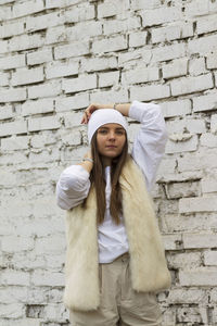 Full length of young woman standing against brick wall