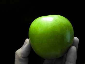 Cropped image of hand holding fruit over black background