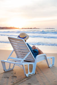 Rear view of woman sitting on chair on beach