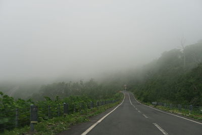 Empty road along trees against sky