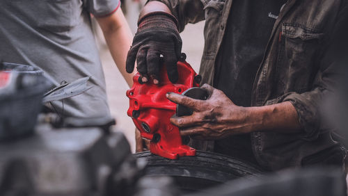 Midsection of people working on car engine in garage