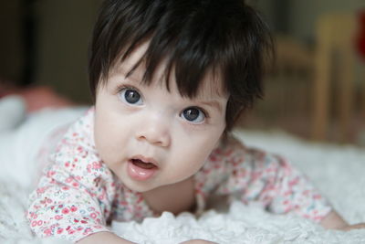 Portrait of cute baby girl lying on bed at home