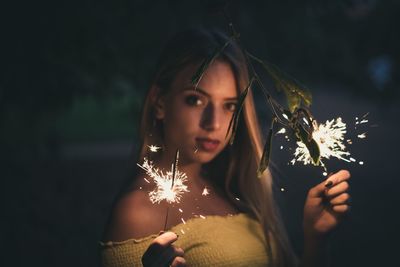 Portrait of young woman holding lit sparkler at night