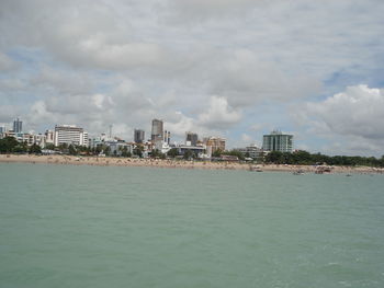 View of city at waterfront against cloudy sky