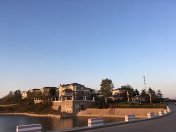 Buildings by river against clear blue sky