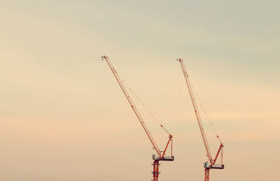 Low angle view of cranes at construction site against sky during sunset