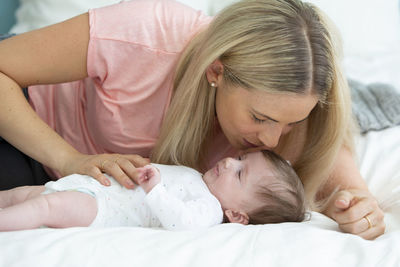 Mother kissing newborn girl on bed at home