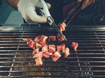 Cropped hands of man cutting meat on barbecue grill