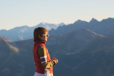 Side view of mature woman standing on mountain against sky