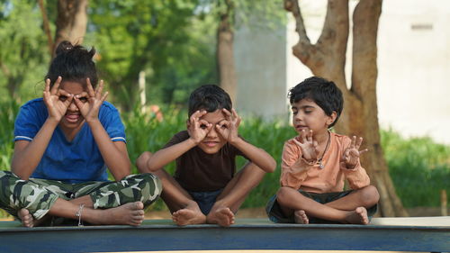 Two indian little girl and a boy doing meditate yoga asana on roll mat with eyes closed in park.