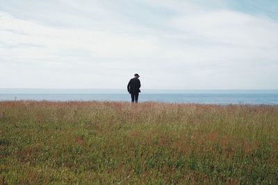 Rear view of man standing on field against sky