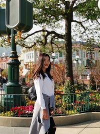 Portrait of young woman standing against trees in city