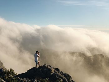 Full length of man photographing landscape against cloudy sky