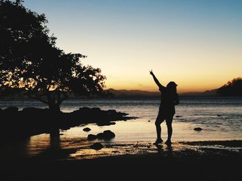 Silhouette man standing at beach against sky during sunset