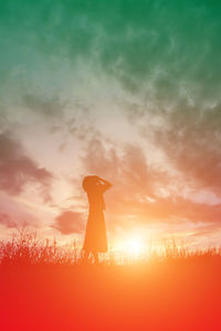 Silhouette woman standing on field against sky during sunset