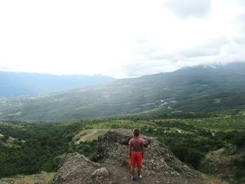 Rear view of boy standing on mountain against sky