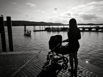 Rear view of young woman with baby stroller standing by sea against sky