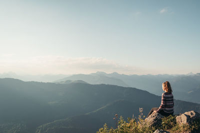 Rear view of man sitting on mountain against sky