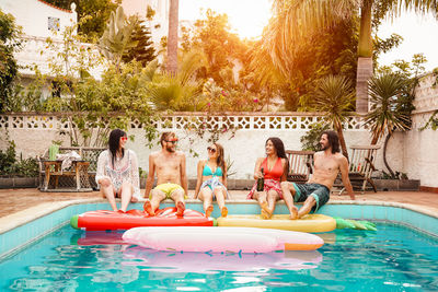 Full length of happy friends sitting at poolside