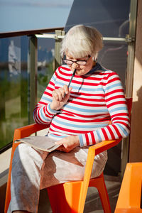 Senior woman in glasses sitting on balcony near the sea