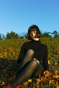 Portrait of young woman sitting on field against clear blue sky