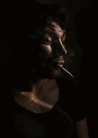 Close-up of man smoking cigarette against black background