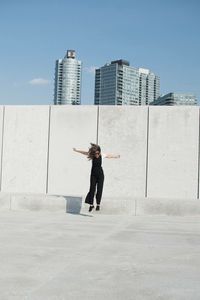 Full length of mature woman with arms outstretched jumping against wall during sunny day