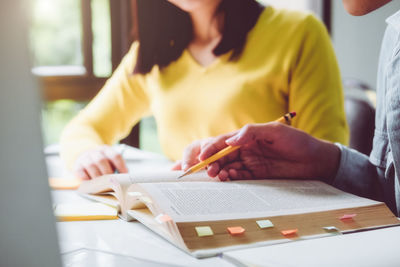 Midsection of woman reading book while sitting on table