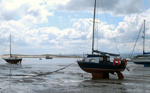 Boats in harbor against cloudy sky