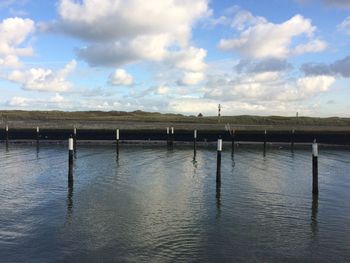 Wooden posts in lake against sky