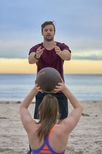 Friends exercising with ball at beach against sky