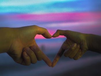 Cropped hands of lesbian couple making heart shape against sky