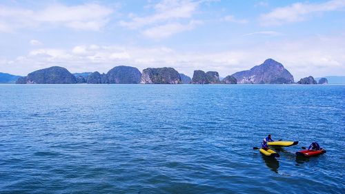 People kayaking in sea against sky