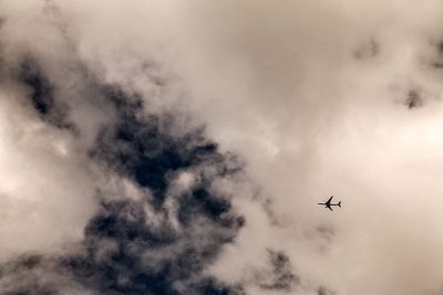 Low angle view of airplane flying against cloudy sky