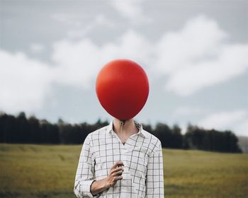 Man holding balloons on field against sky