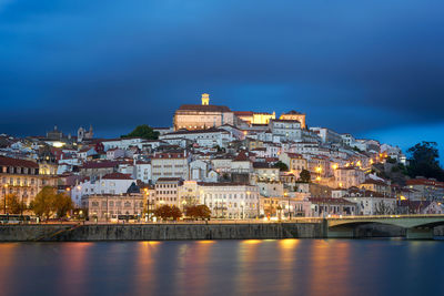 Illuminated buildings by river at dusk