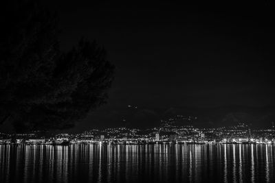 Illuminated trees by river against sky at night