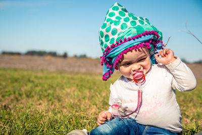 Girl with pacifier looking away while sitting on grass against sky