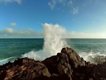 Waves splashing on rocks at shore against sky