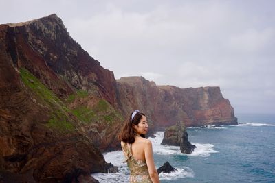 Portrait of young woman on rock by sea against sky