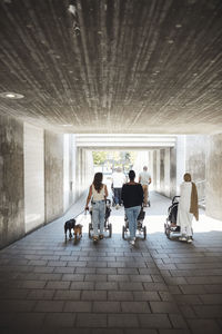 Rear view of mothers walking with baby strollers through underpass