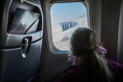 Rear view of girl looking through window of airplane