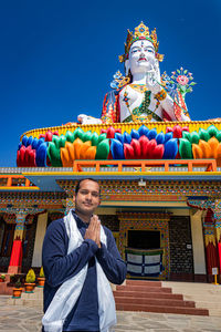 Young man praying in front of buddhist colorful goddess statue with blue sky at morning