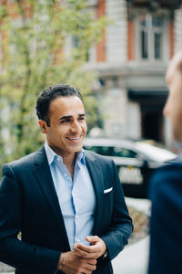 Smiling businessman looking away while standing in city