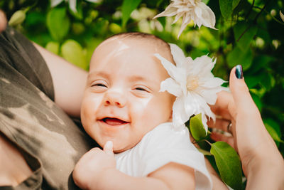 Midsection of mother holding cute baby boy by flower