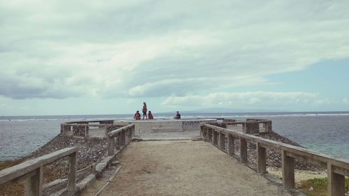 People on pier over sea against sky