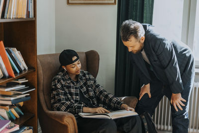 Young male student showing book to professor in library