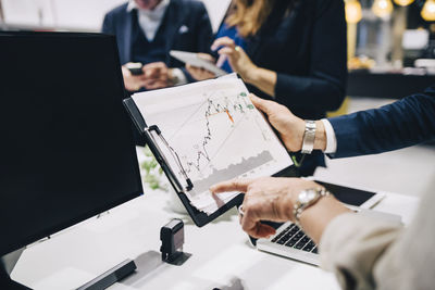 Cropped image of business partners analyzing graph in meeting room at office